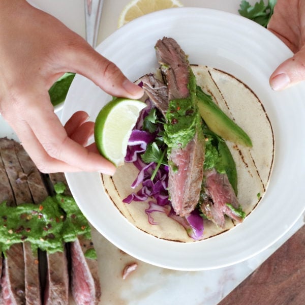 Registered Dietitian Lindsay Pleskot holding a lime wedge over a round white plate topped with grilled steak chimichurri.