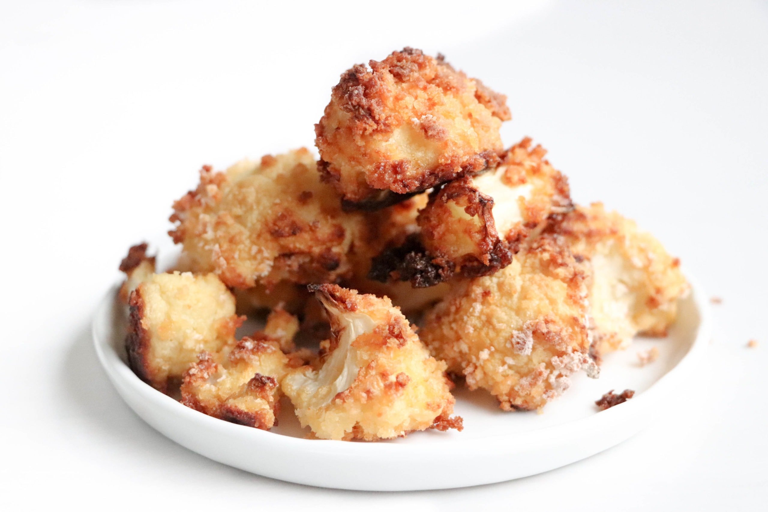 Crispy baked cauliflower on a white plate over a white surface.