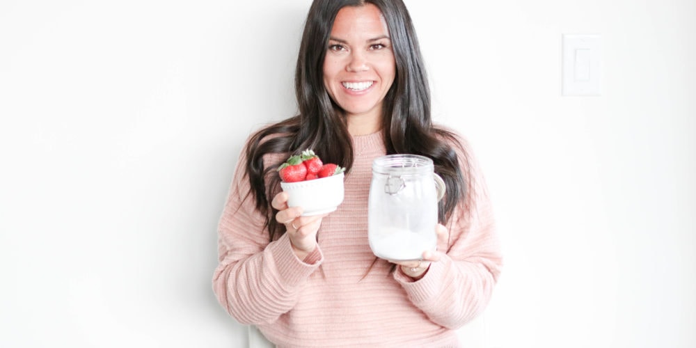 Holding a white bowl filled with strawberries in one hand and a jar of white sugar in the other hand.