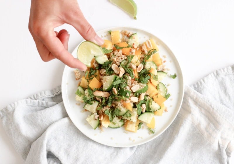 Hands holding up a white plate serving thai turkey and quinoa salad topped with fresh mint, cucumber and yellow peppers. A Recipe by REgistered Dietitian Lindsay Pleskot