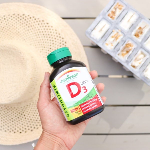 Lindsay Pleskot, RD holding a bottle of Jamieson Vitamin D supplements over a picnic bench with a hat and popsicles.