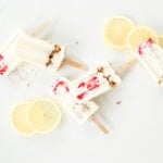 3 ingredient high protein lemon cheesecake smoothie pops laid out on a white surface surrounded by lemon slices.