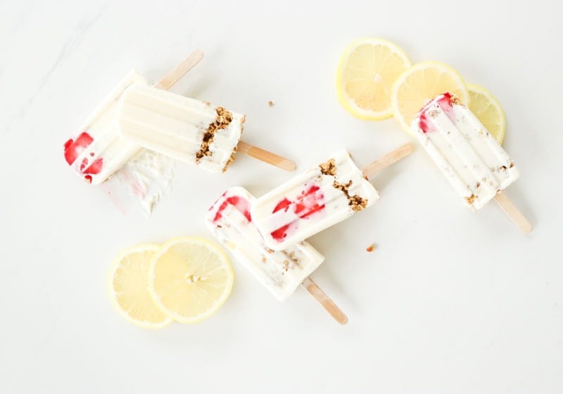 3 ingredient high protein lemon cheesecake smoothie pops laid out on a white surface surrounded by lemon slices.