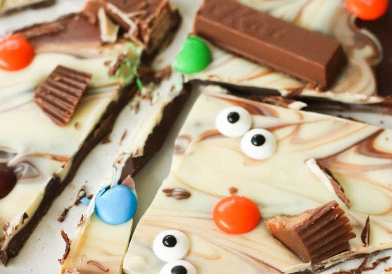 close up shot of DIY chocolate Halloween Bark decorated with candy monster eyes, kitkat bars, M&Ms and reeses peanut butter cup. Recipe by Lindsay Pleskot Registered Dietitian