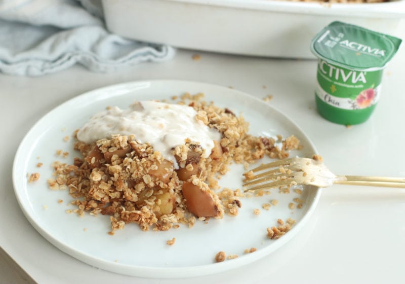 Baked breakfast apple crisp on a white plate topped with Activia Chia yogurt with a gold fork. Ingredients include: oats, almond flour, coconut oil, cinnamon, chia seeds, Activia Chia Probiotic Yogurt.
