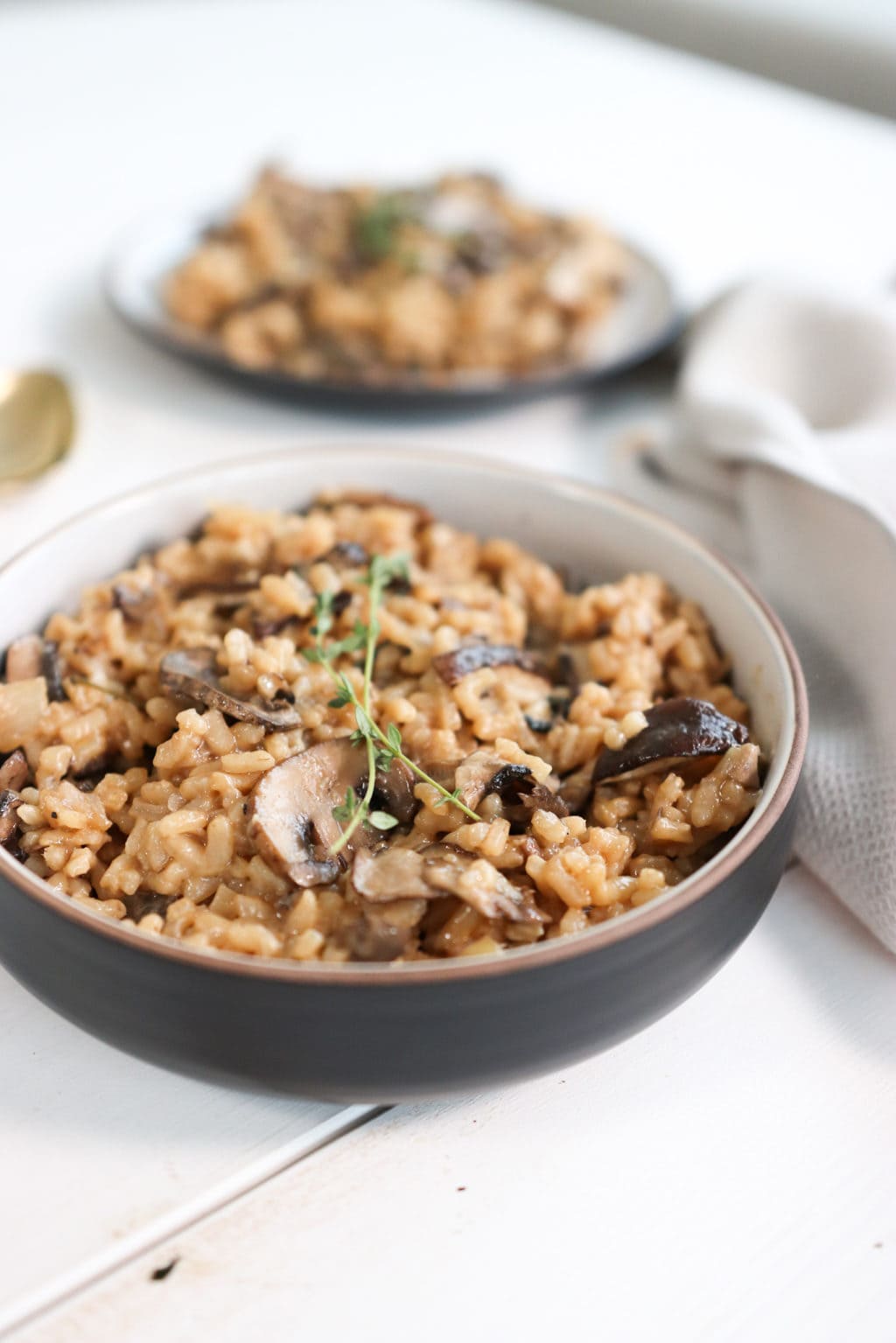 Creamy mushroom risotto in a white and brown bowl over a white food board. Ingredients include: mushrooms, garlic, parsley, arborio rice, white wine, vegetable stock, parmesan, butter