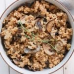 Creamy mushroom risotto in a white bowl over a white food board. Ingredients include: mushrooms, garlic, parsley, arborio rice, white wine, vegetable stock, parmesan, butter