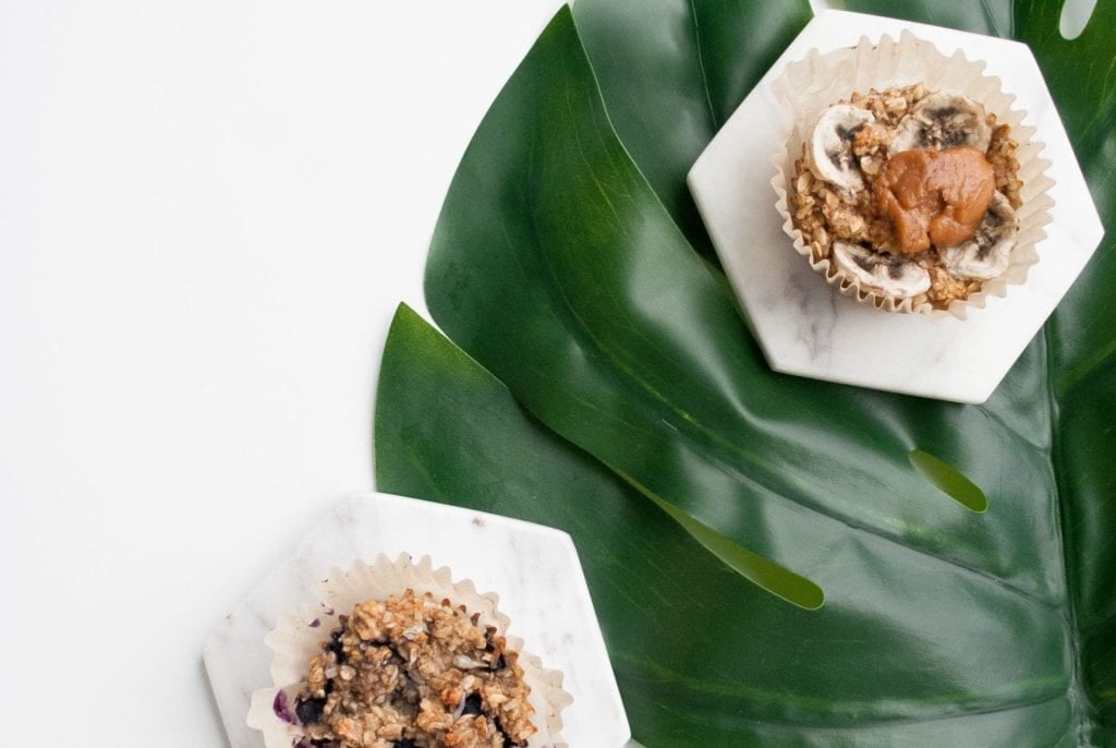 Oatmeal cups on a white surface over a green leaf. Ingredients include oats, banana, natural peanut butter.