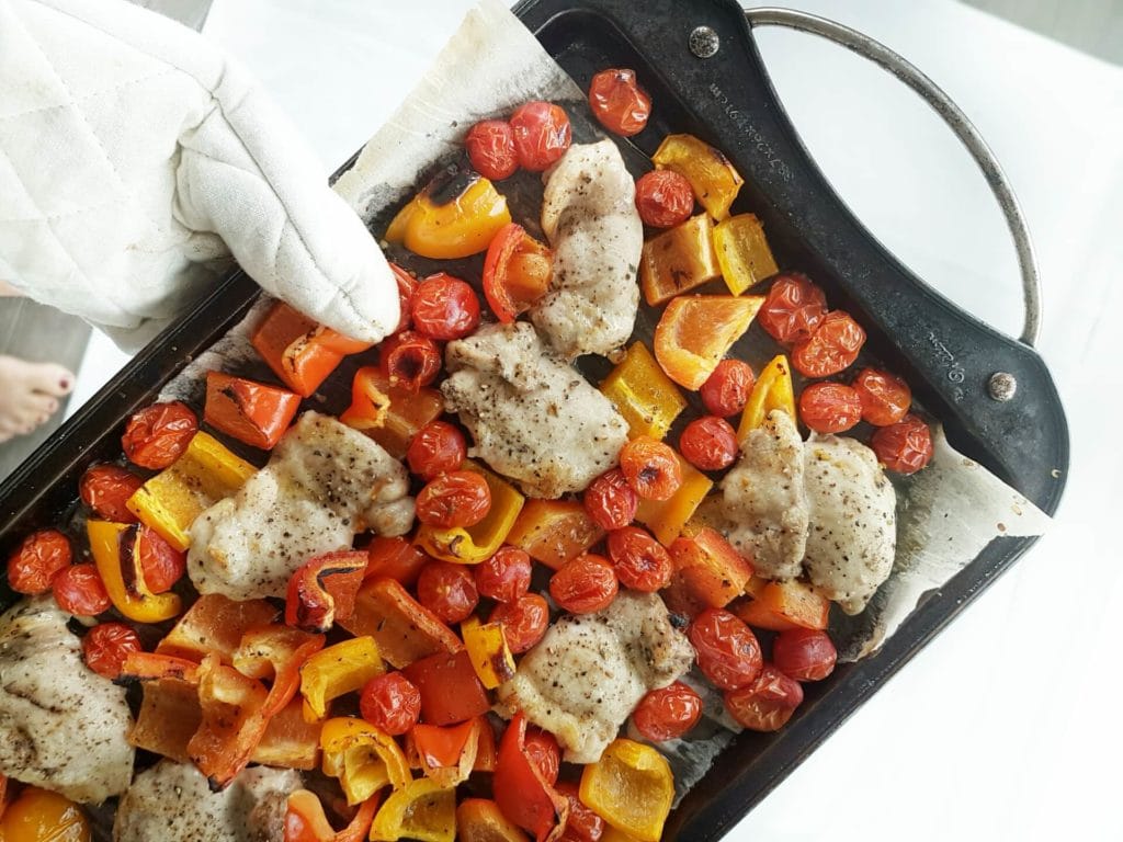 One pan chicken with blistered tomatoes and red peppers over a white surface.