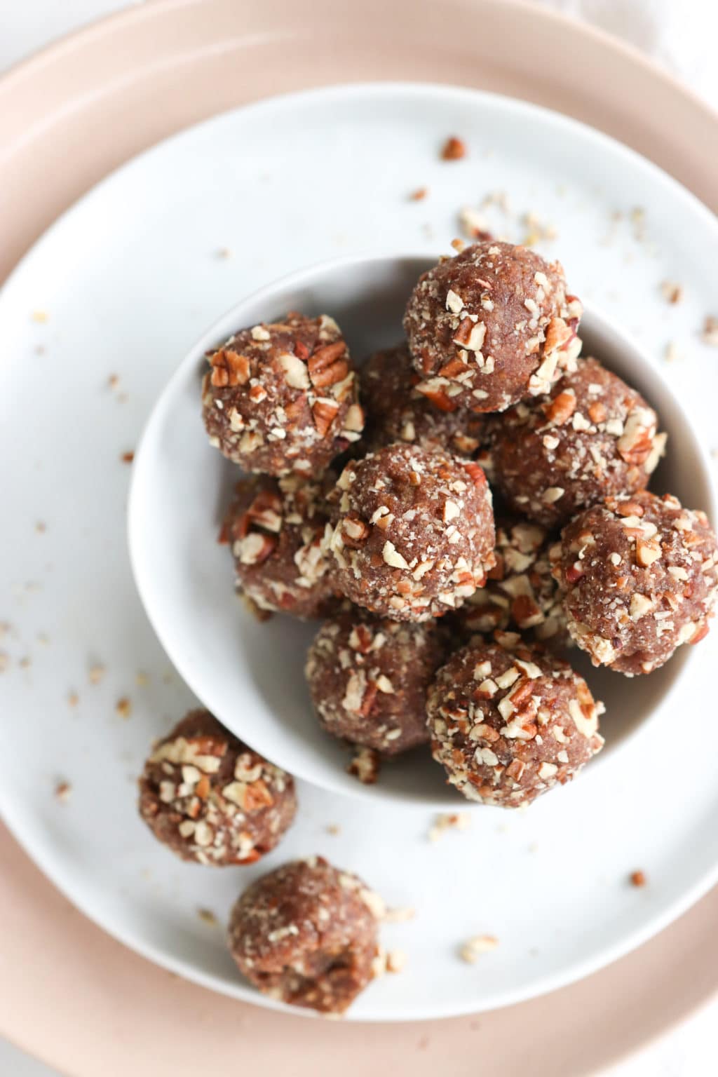 Pecan Pie Energy Balls in a bowl over a pink and white plate. Ingredients include: pecans, dates, vanilla, salt, cinnamon.