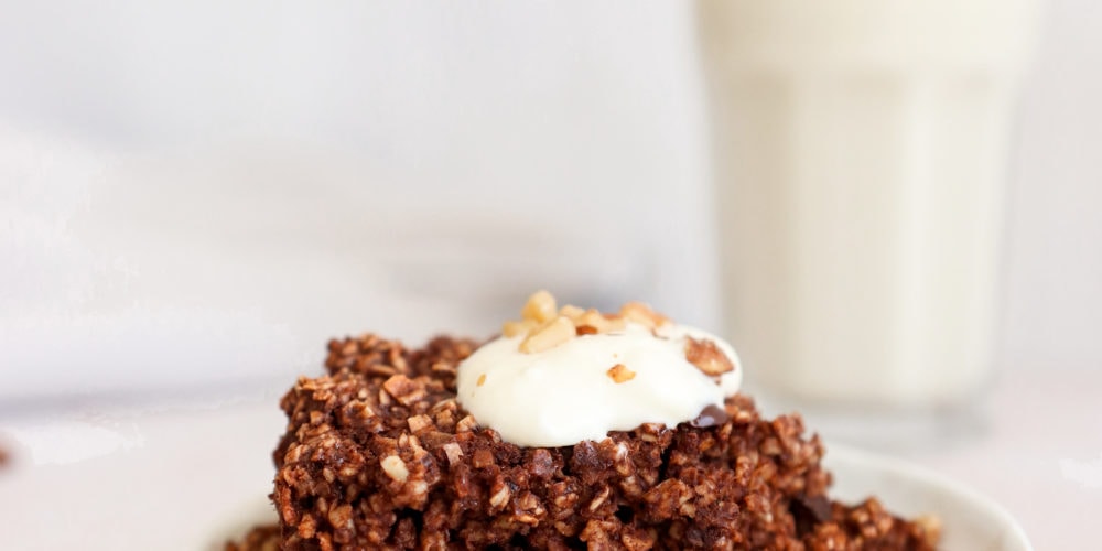 A serving of chocolate baked oatmeal on a white plate in front of a glass of milk.