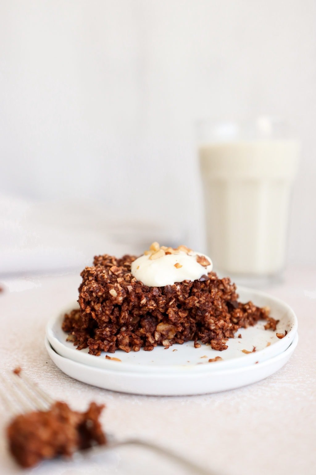 Chocolate baked oatmeal on two white plates with a glass of milk behind it. Ingredients include: oats, banana, egg, coconut oil, maple syrup, cinnamon, prunes, walnuts.