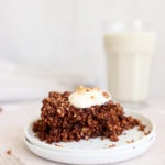 A serving of chocolate baked oatmeal on a white plate in front of a glass of milk.