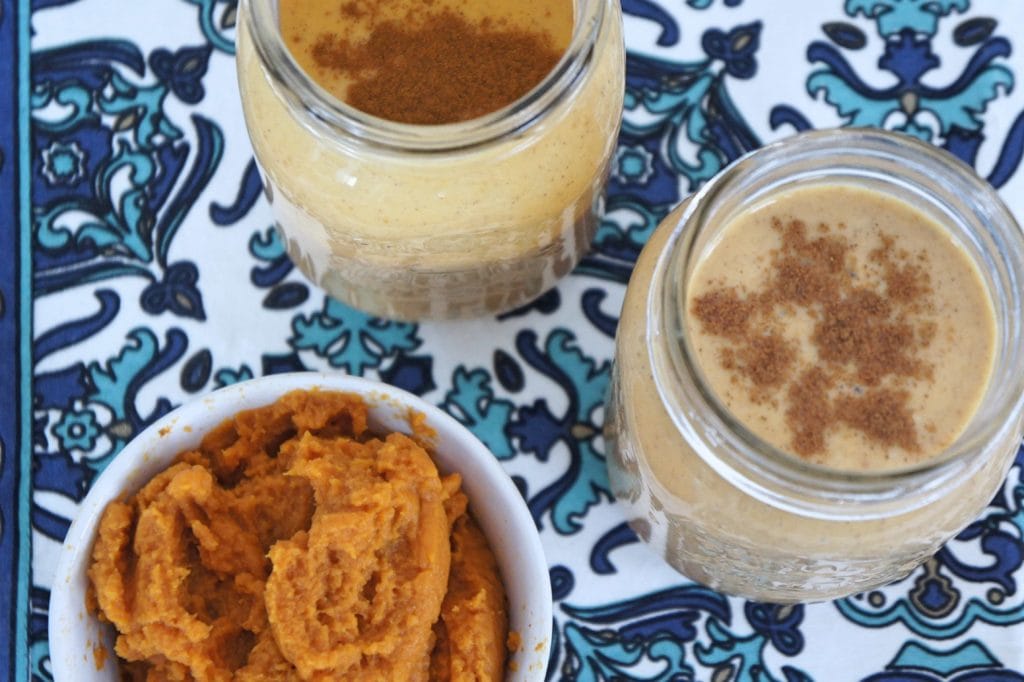 Two Creamy Pumpkin Spice Smoothies in mason jars over a blue and white pattern surface.