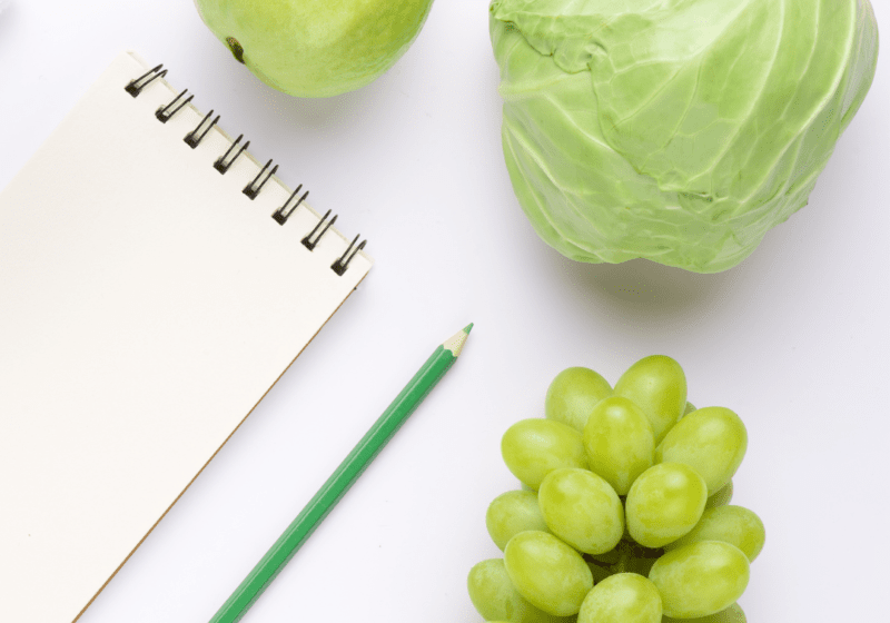 Image of an apple, cabbage and grapes with a notepad and pencil in the corner