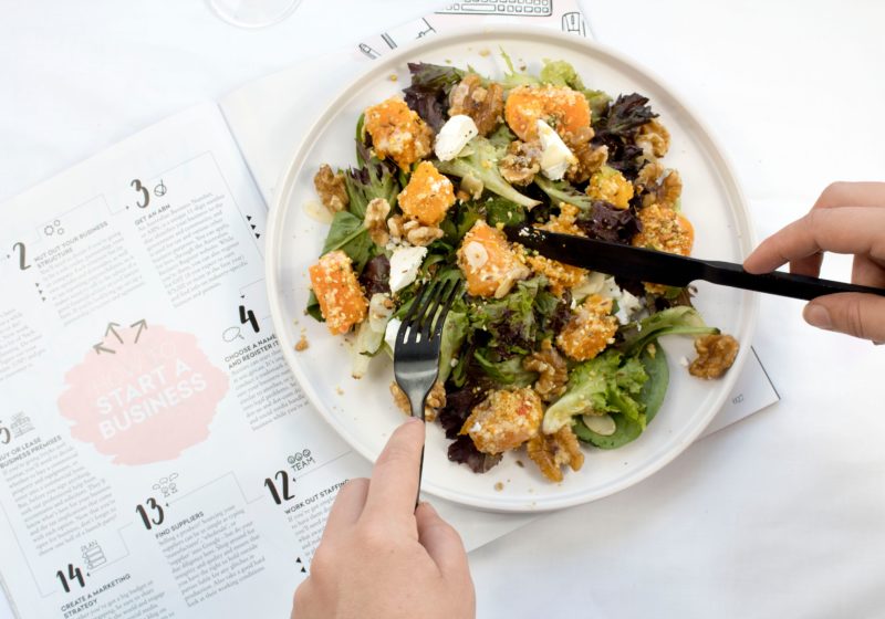 Image of someone's hands using a fork and knife to eat their salad over a calendar