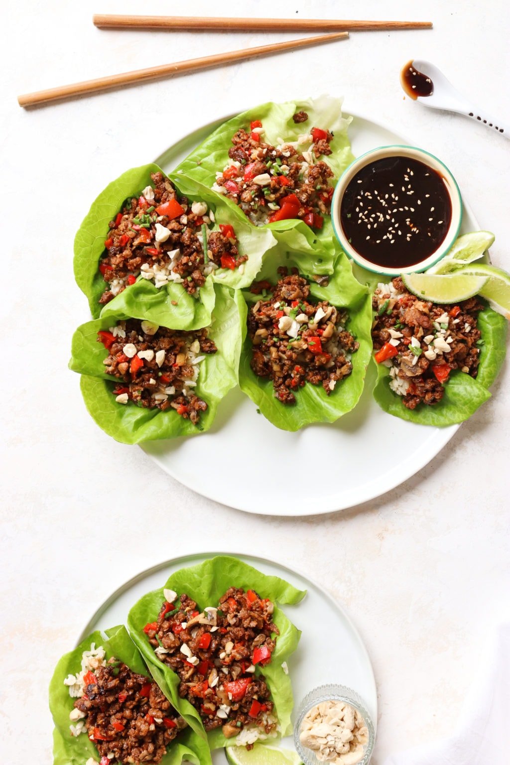 A white plate of 5 open face lettuce wraps and a small bowl of hoisin. At the top of the photo are chop sticks and a white spoon dripping with hoisin. 
