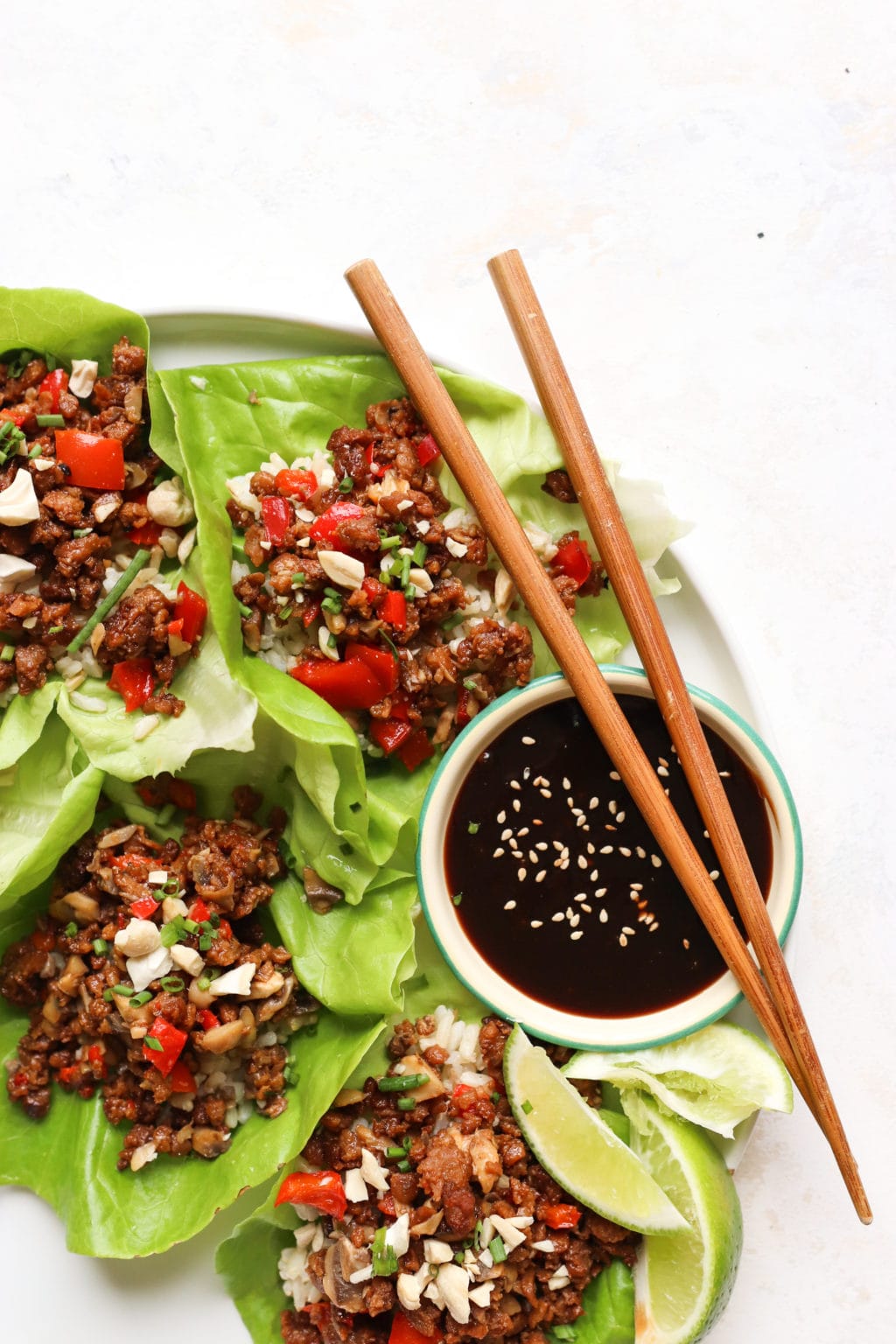 A photo of half a white plate zoomed into 3 open face lettuce wraps with a small bowl of hoisin. 2 chop sticks are on top of the bowl of hoisin.