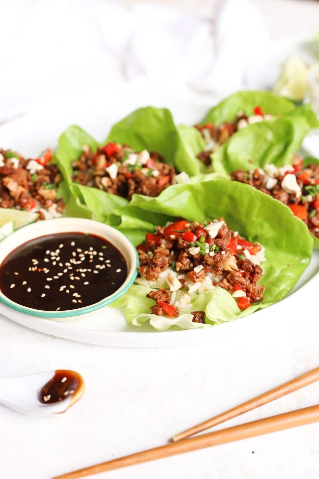 A photo of half a white plate zoomed into 3 open face lettuce wraps with a small bowl of hoisin.