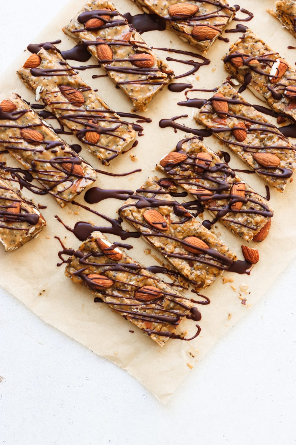 9 no-bake granola bars topped with almonds and chocolate drizzle are on a piece if parchment paper