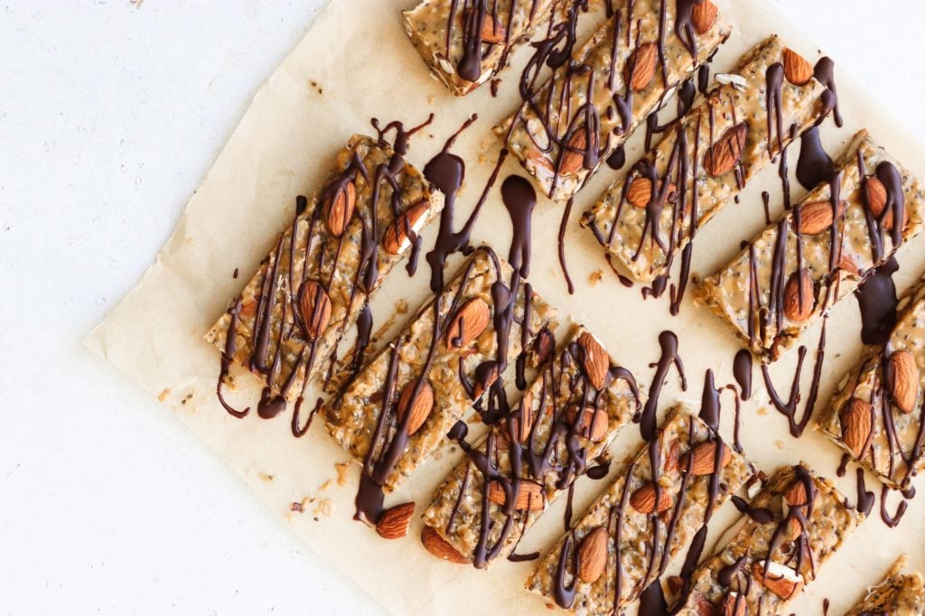 no-bake granola bars topped with almonds and chocolate drizzle are on a piece if parchment paper