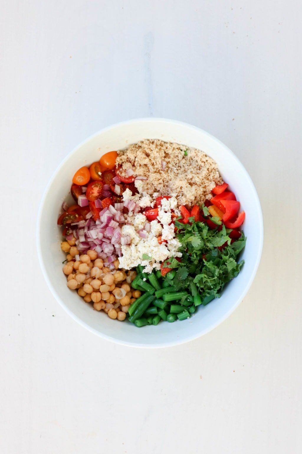 A bowl of quinoa, tomatoes, chickpeas, feta, green beans, red onions and red peppers in a bowl.