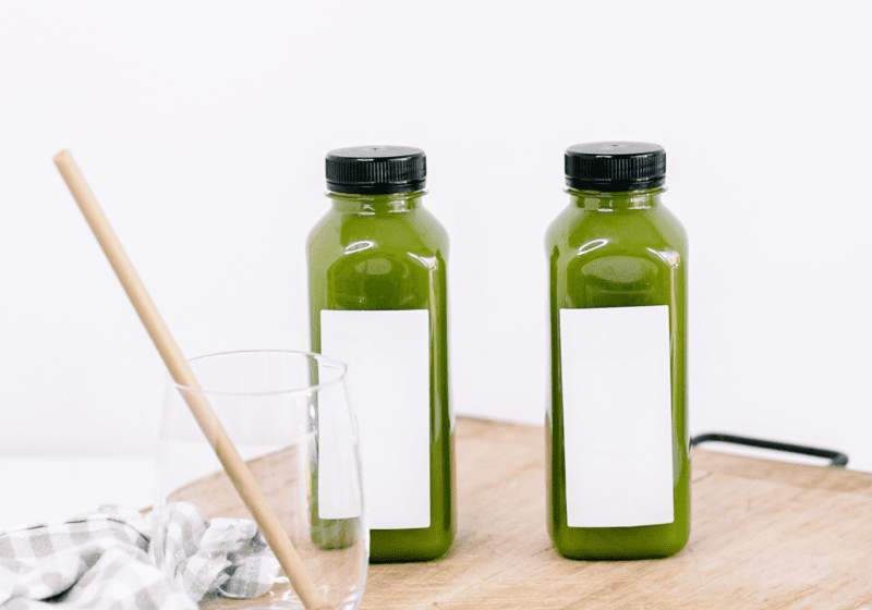 Two bottles of green juice are on a cutting board