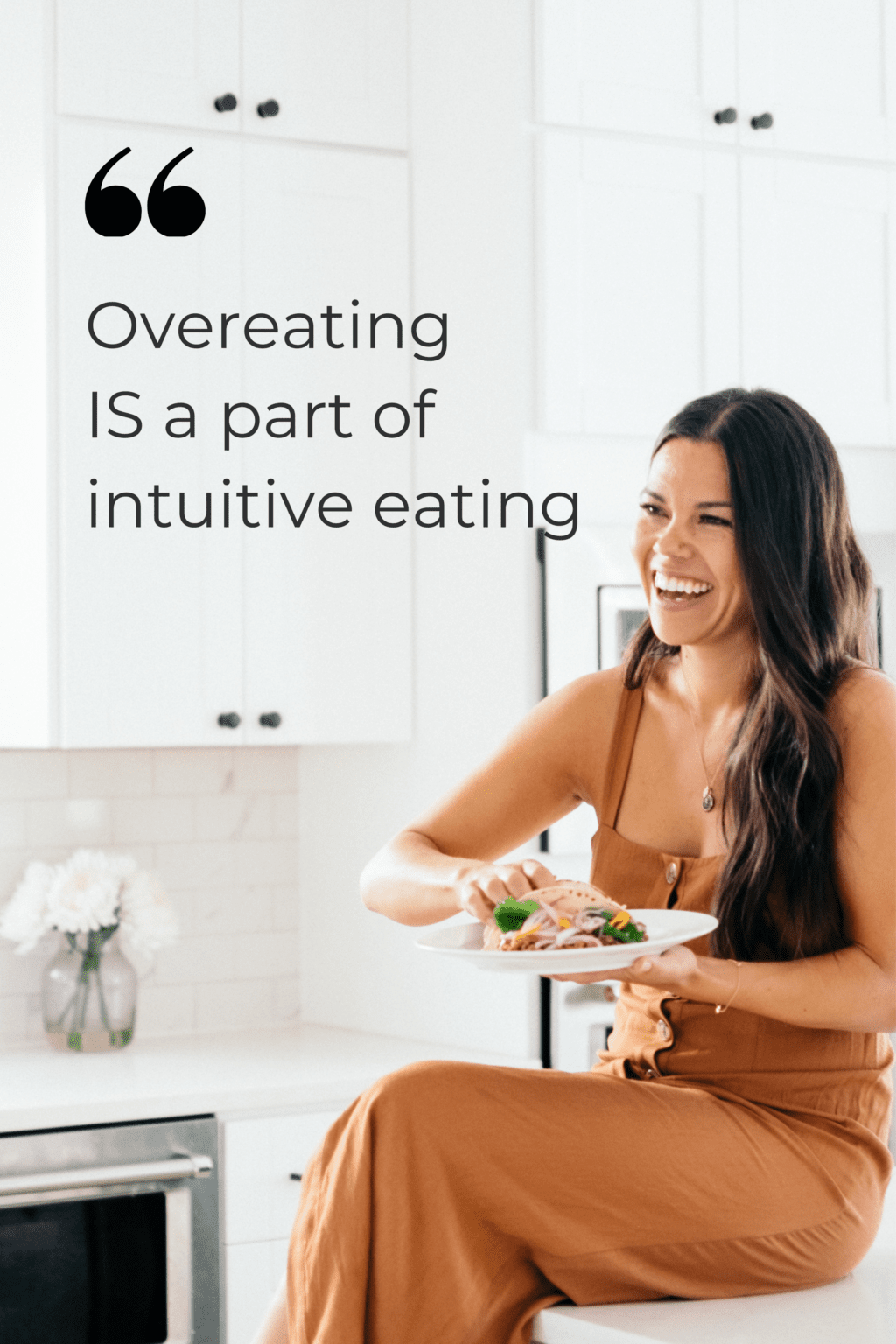 A woman with black hair is sitting on a counter in a brown dress. She is in a white kitchen eating a taco. There is text overlay to the left of the girl that reads "overeating is a part of intuitive eating".