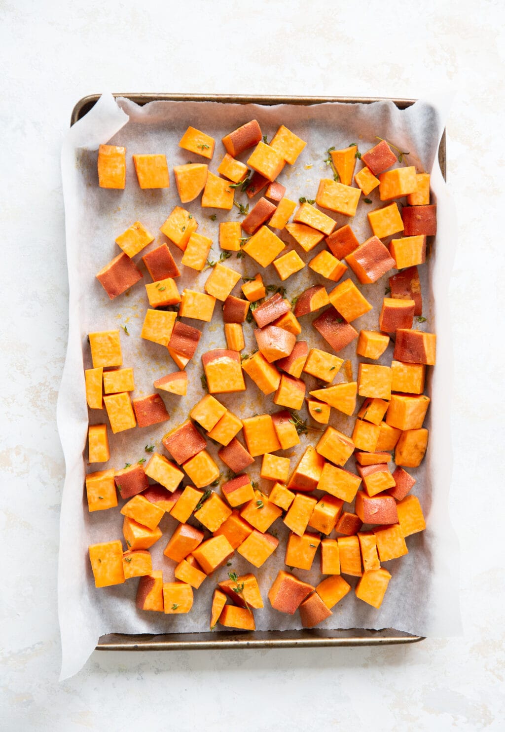 Cubed sweet potatoes are on a baking sheet that is lined with parchment paper.