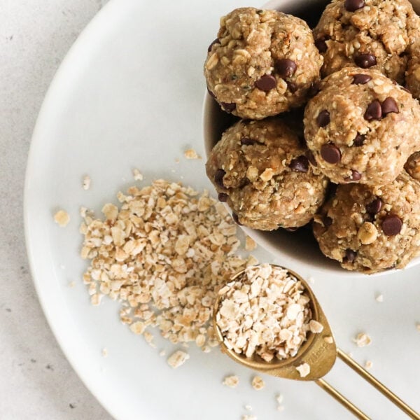 A tablespoon of oats is beside a bowl of energy bites both are on a white plate.