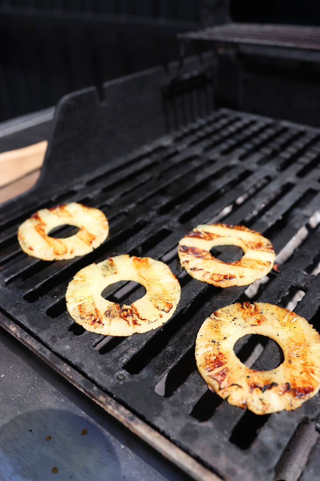 grilled pineapple rings sit on a black barbecue grate
