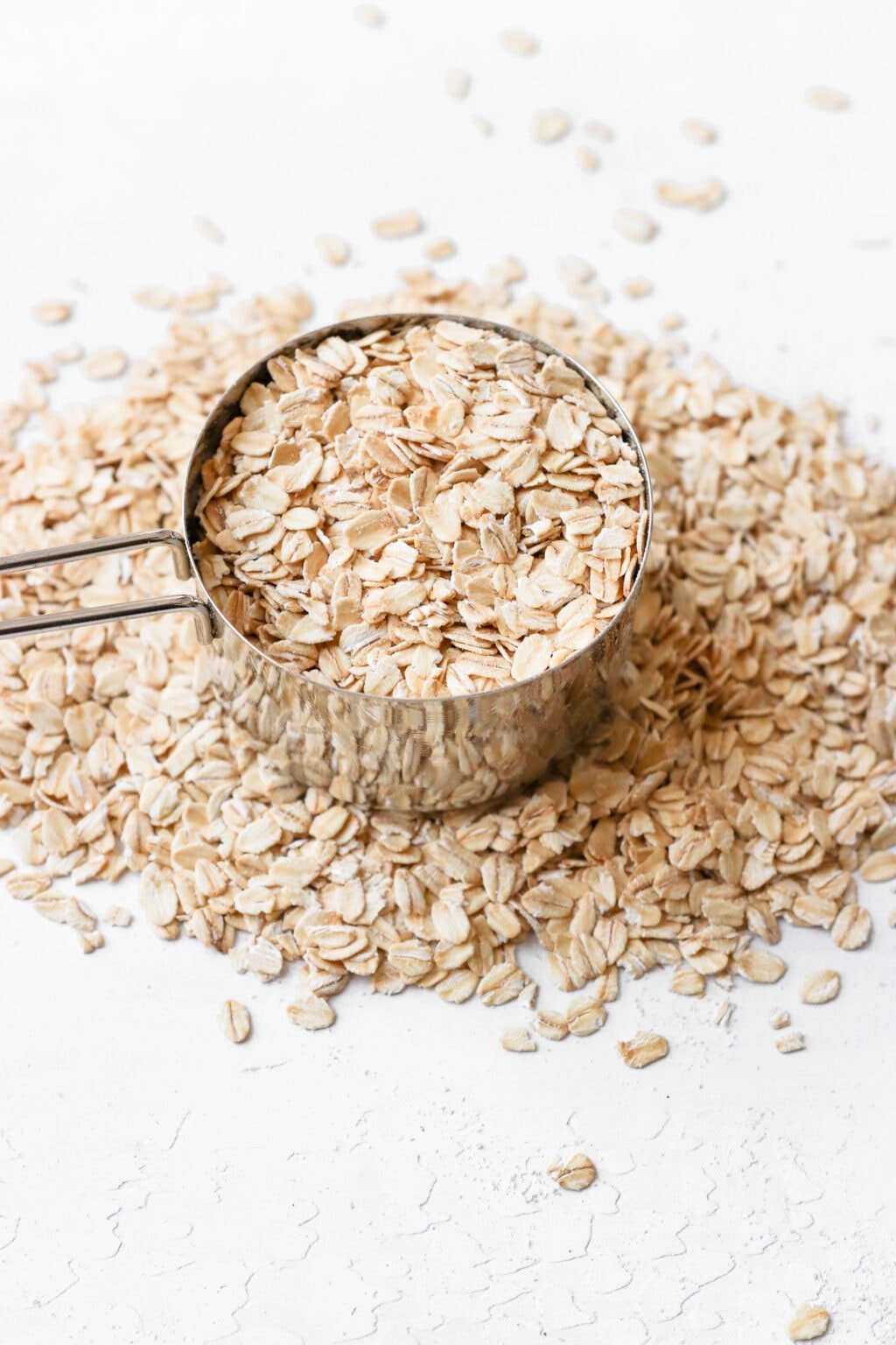 A silver 250 mL measuring cup is filled to the brim with quick oats. There are quick oats on the counter spilling over surrounding the measuring cup.