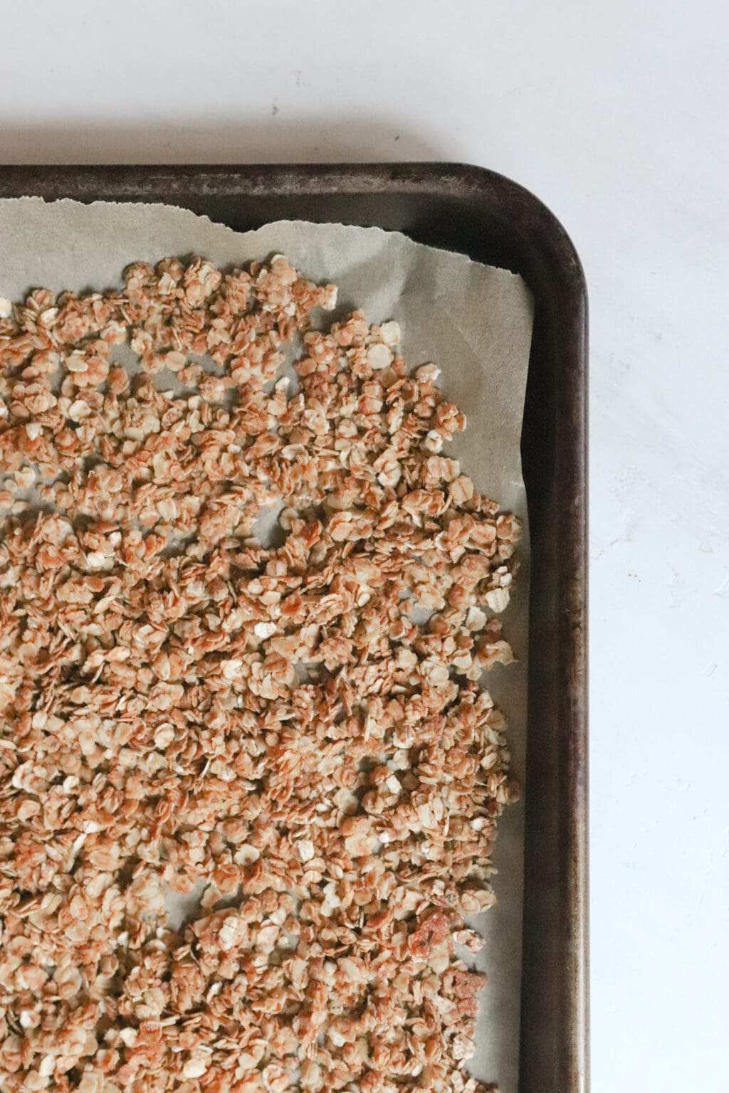 The image shows 3/4 of a baking sheet lined with parchment paper has golden oats evenly distributed across the pan.  
