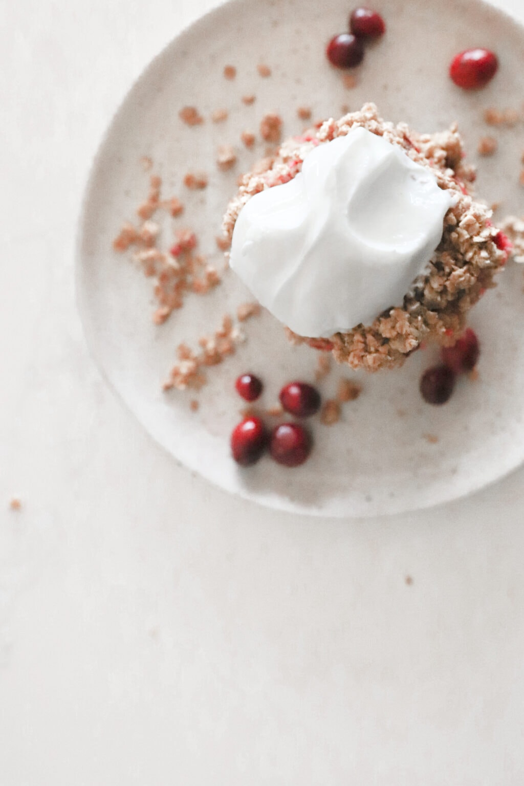 A grey plate has a cranberry oat bars stacked on top of each other and is topped with greek yogurt. The bars are surrounded by oat crumble and fresh cranberries.