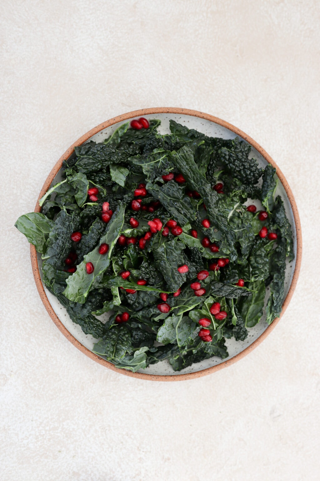 A speckled grey bowl with a brown rim has town dine kale in it and pomegranate arils (or seeds).