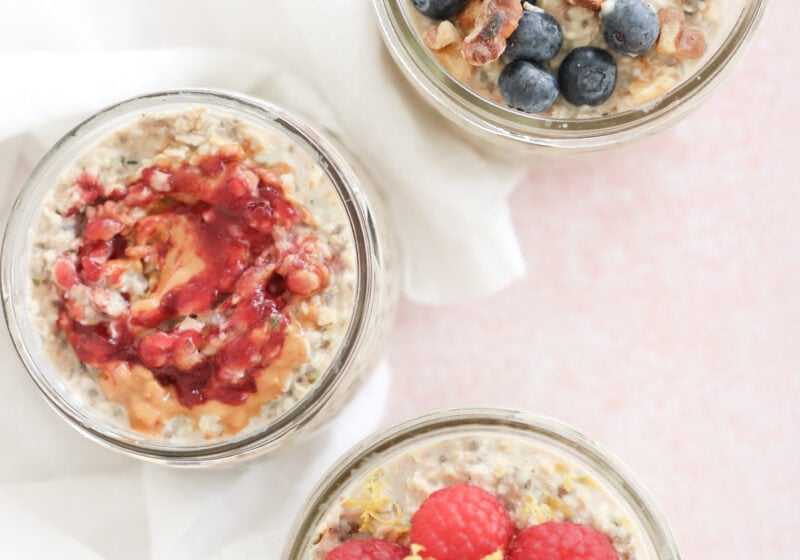 The simple overnight oats base recipe is divided into 3 small mason jars. One is topped with blueberries and toasted walnuts, one is topped with raspberries and lemon zest and one is topped with peanut butter and jelly