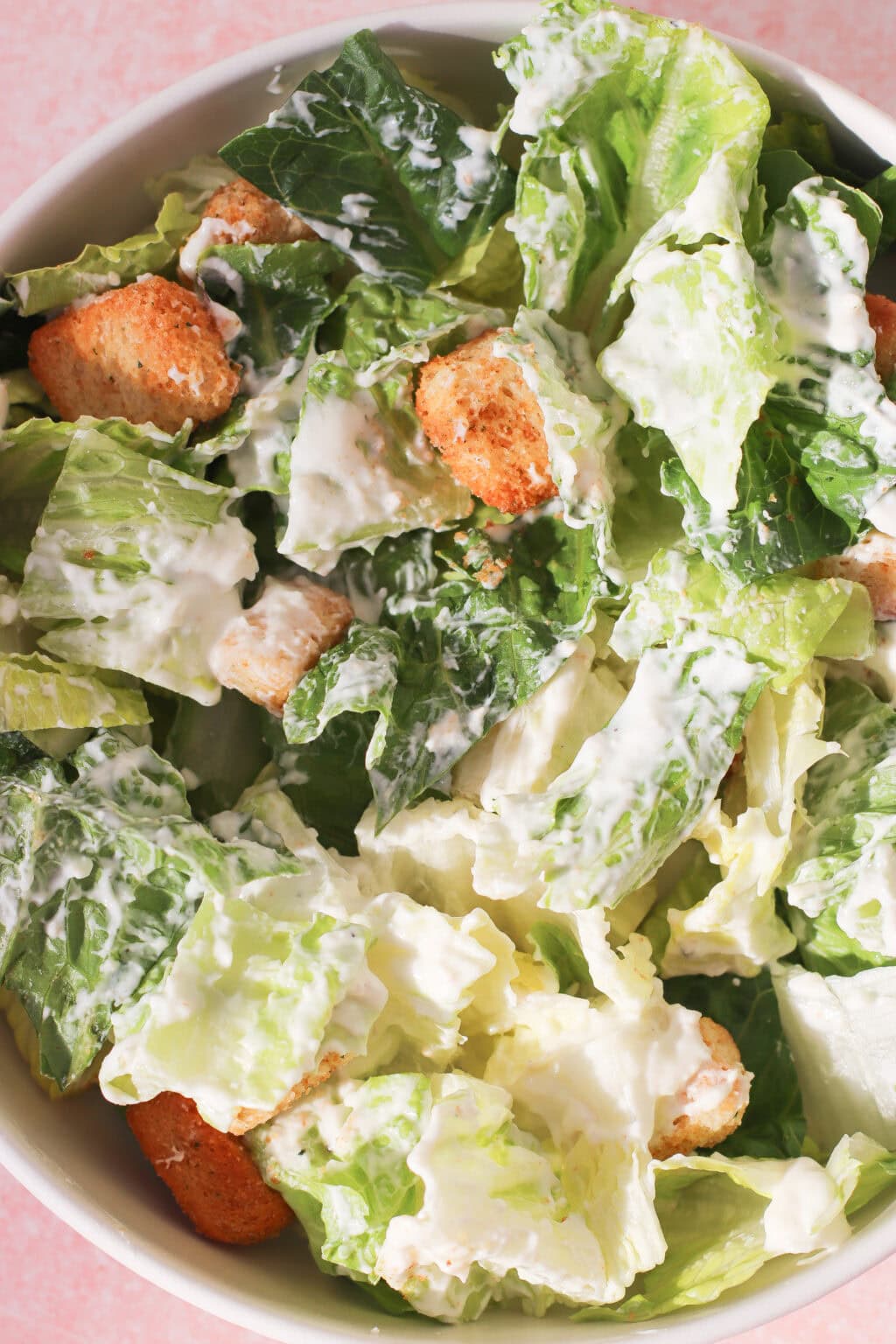 A close-up of a Caesar salad with crisp romaine lettuce, golden croutons, and creamy Caesar dressing with Greek yogurt in a white bowl.