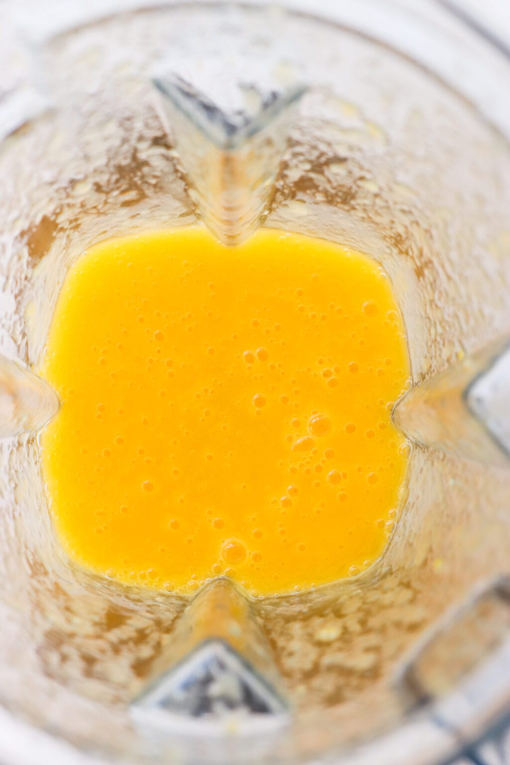 An overhead shot of a blender with a yellowish orange mango puree in it