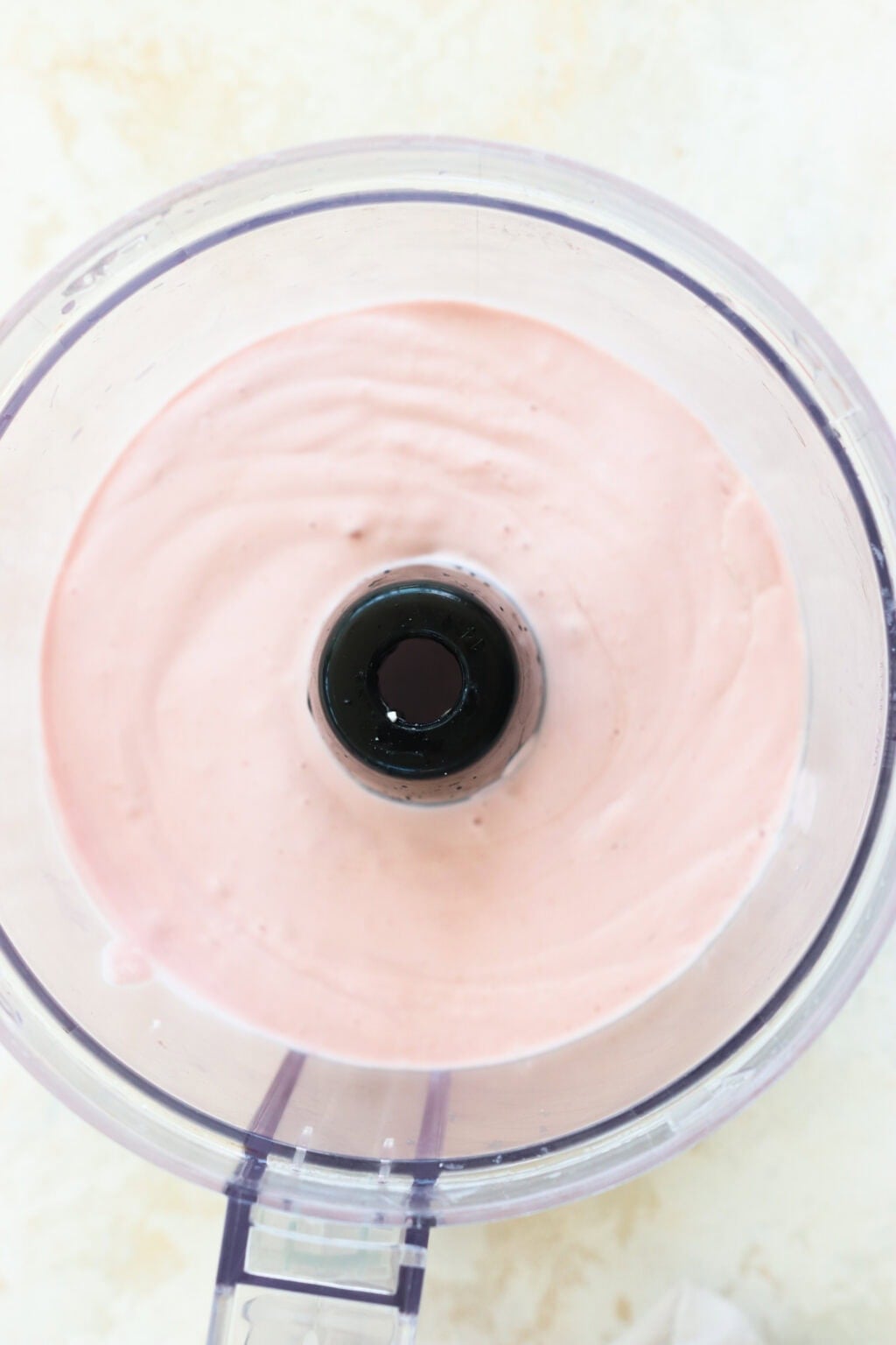 a smooth light pink mixutre of blended cottage cheese ice cream in an open food processor on a white background