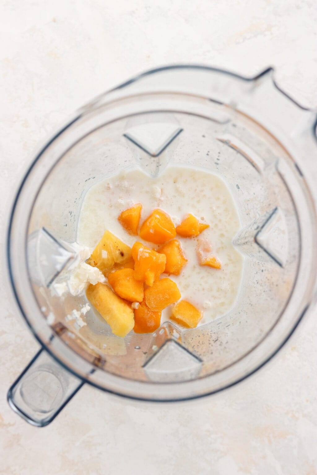 This is an overhead shot of ingredients in a vitamix blender before it's blended. There is milk, yogurt and mango in the blender.