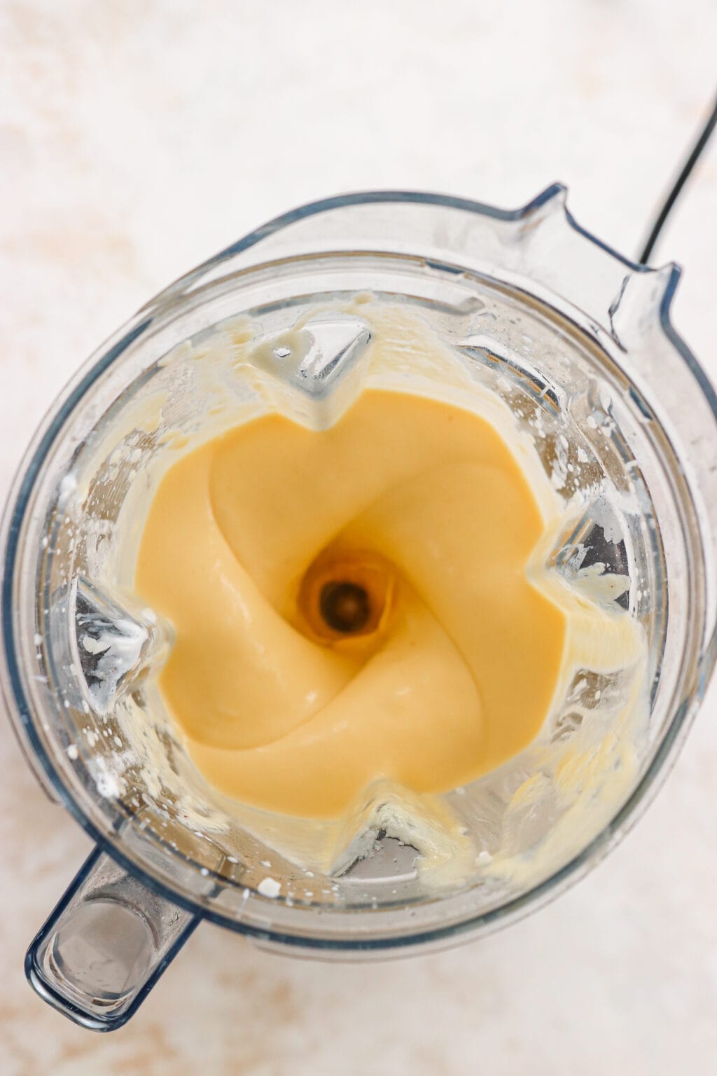 This is an overhead shot of a mango and pineapple smoothie being blended in a vitamix. The smoothie is orange in color and there are splashes of smoothie on the sides.