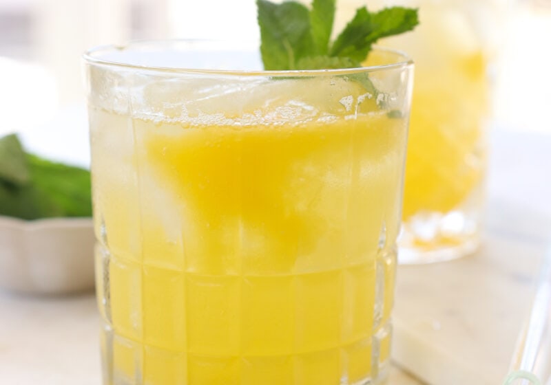 A glass is filled with soda water and topped with a yellowish-orange puree. The glass is garnished with mint. In the background is the same glass with mint blurred out.