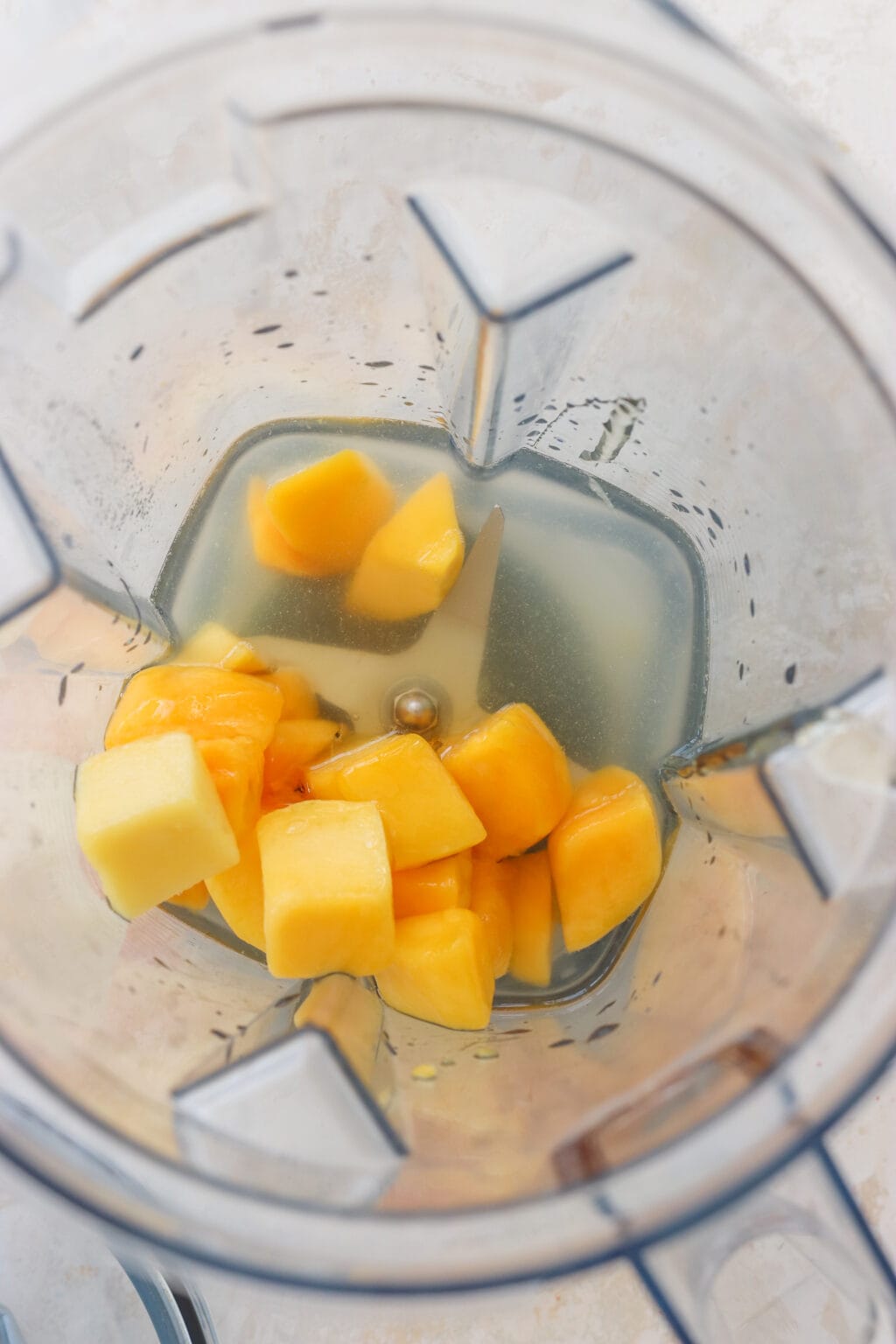 An overhead shot of inside a blender. There is mango, water, and lime juice.