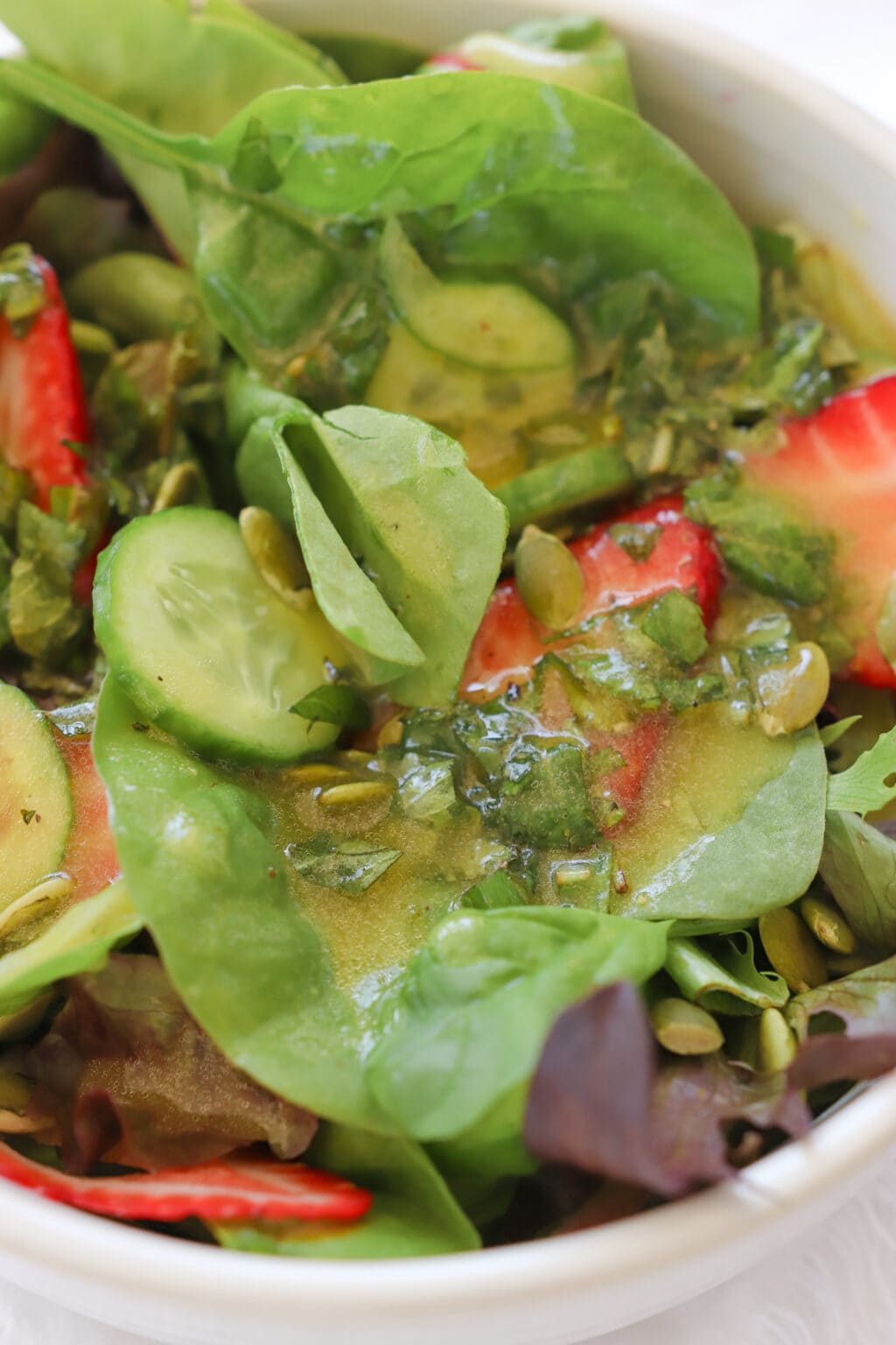 A zoomed in photo of a mixed green salad with strawberries dressed in yellow vinaigrette.