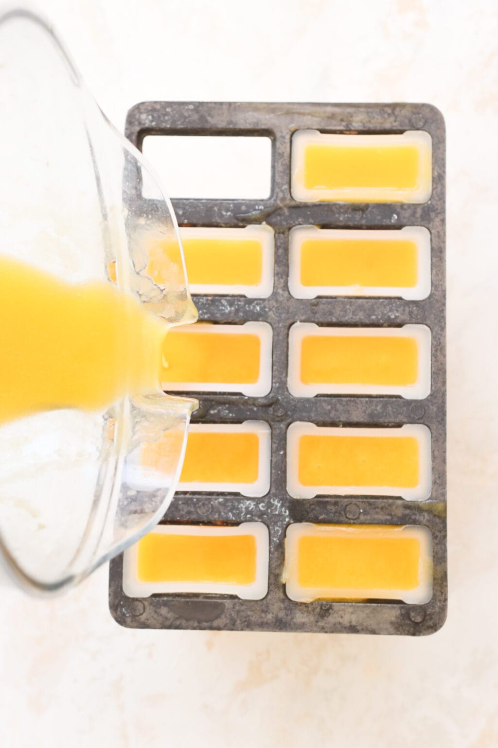 An overhead photo of a blender pouring an orange yellow liquid into popsicle molds.