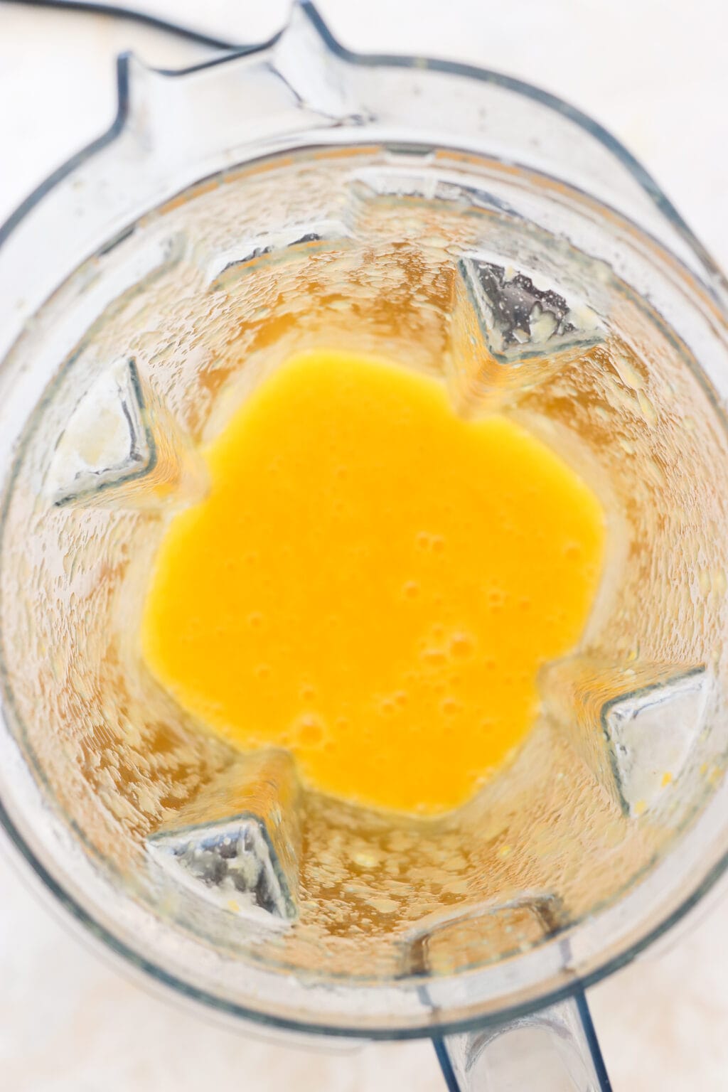 An overhead shot of a  blender with orange yellow liquid in it, bubbling.