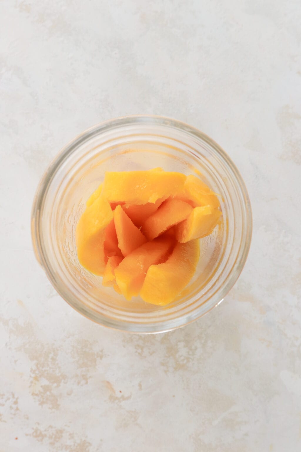 An overhead shot of a mason jar with 10 slices of mango in it. 