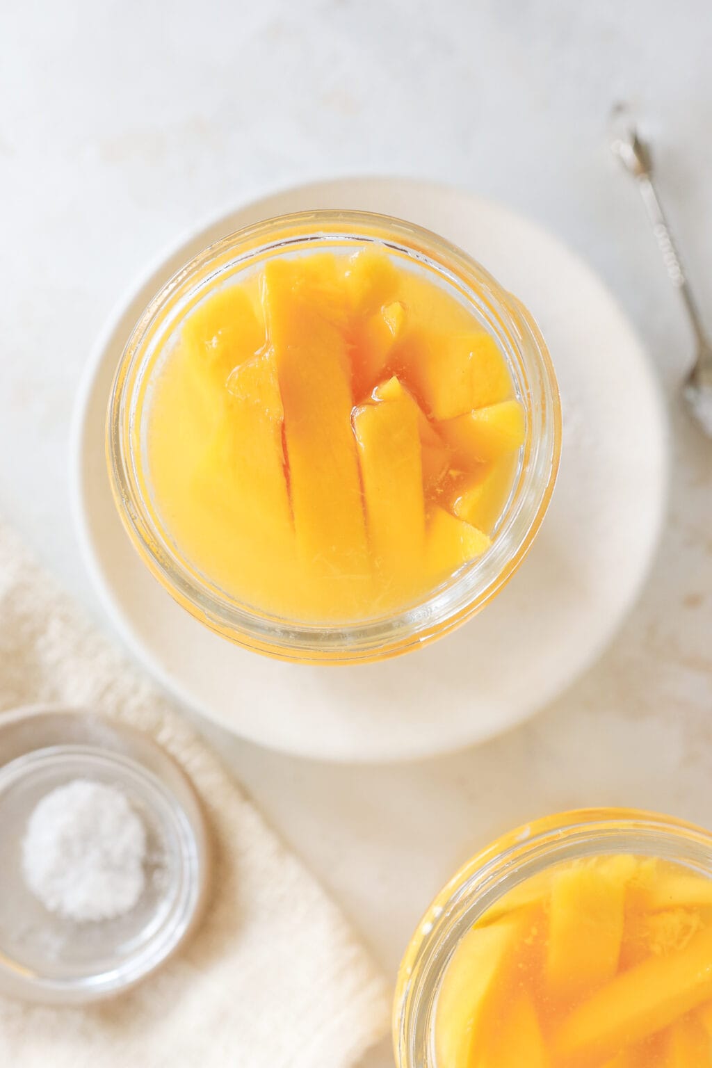 An overhead shot of a jar with a mango in it. The jar has water in it and there is a bowl of salt in the corner.