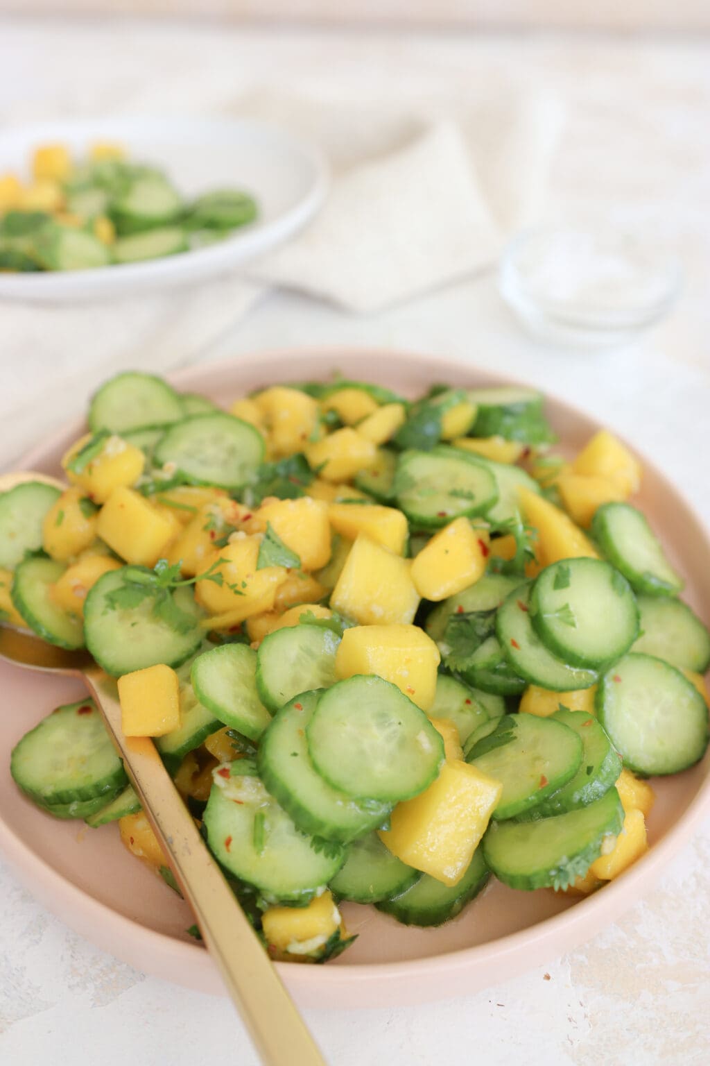 A pink plate has a serving of cucumber and mango salad. There is gold cutlery on it.