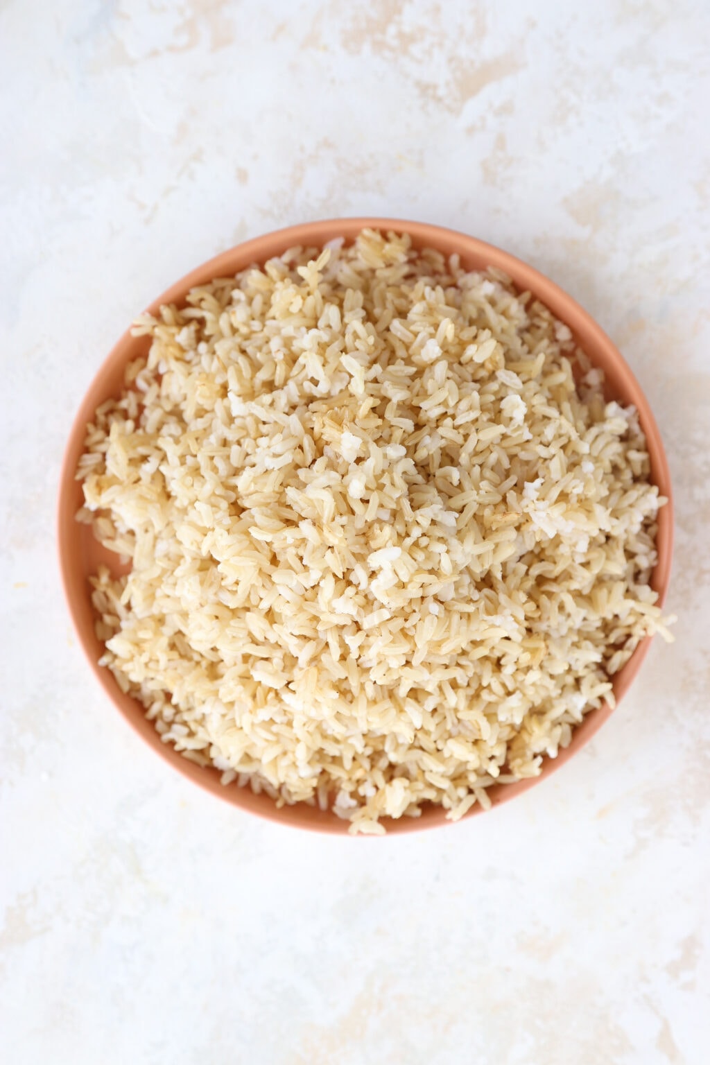 A brown rimmed plate is filled with cooked brown rice.